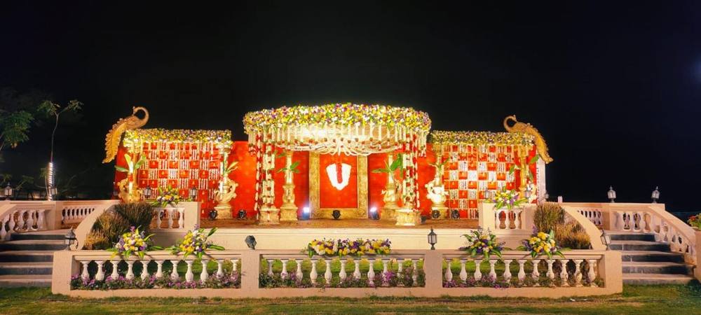 Outdoor wedding stage with peacock accents and red and gold backdrop